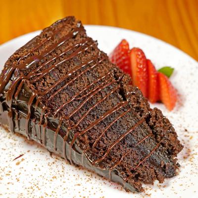 A slice of rich chocolate cake with chocolate icing and a strawberry garnish.