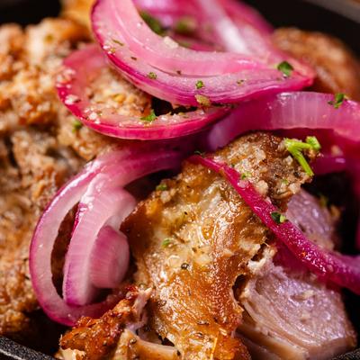 Fried pork chunks topped with red onion, an appetizer dish, close up.