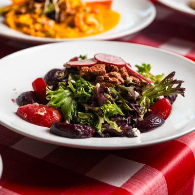 Beet salad on a white plate, set on a red checkered tablecloth with other dishes.