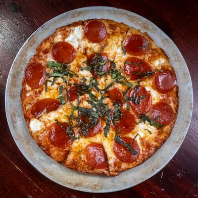 Overhead view of a small pepperoni pizza with basil garnish on a metal tray.