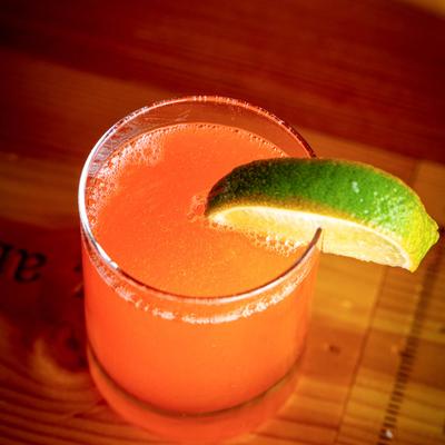 A glass of orange cocktail garnished with a lime slice rests on a wooden surface.