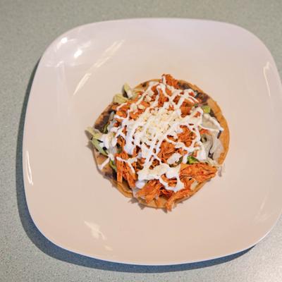 Tostada featuring shredded chicken, lettuce, crema and grated cheese.