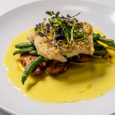Gourmet dish - fish, green beans, potatoes, microgreens and yellow sauce on a white plate.