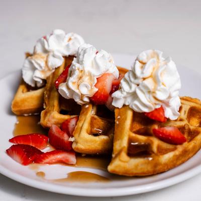 Waffles with whipped cream, syrup, and strawberries.