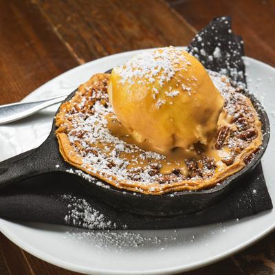 Pecan pie in a skillet with ice cream, dusted with powdered sugar.