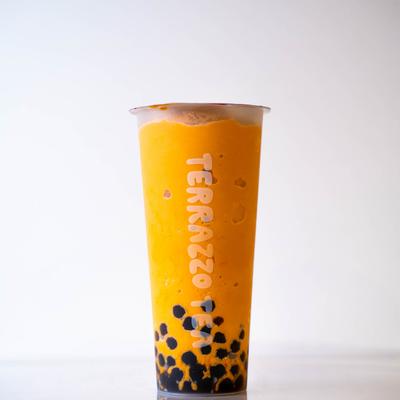 A tall, clear cup of vibrant orange bubble tea with a layer of black tapioca pearls at the bottom.