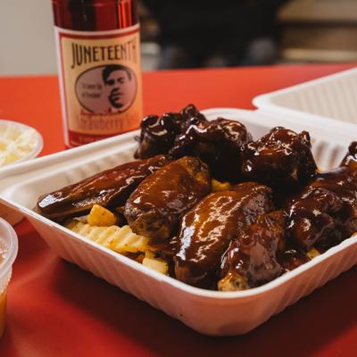 BBQ chicken wings and fries with a jar of Juneteenth sauce in the background.