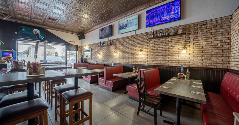 Interior of a restaurant with red booths, brick walls and TVs on the wall.