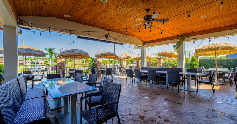 Outdoor restaurant patio with wicker furniture, straw-thatched umbrellas
