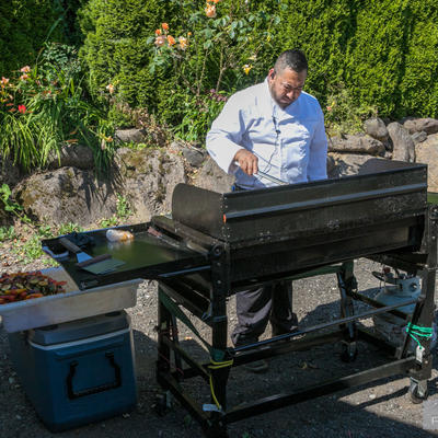 Employee working on barbecue with garden in the back
