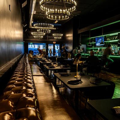Dim dining room with chandeliers and a glowing green bar.