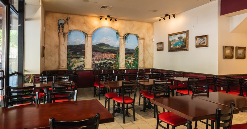Interior of a restaurant with red cushioned chairs, wooden tables, and a large landscape mural