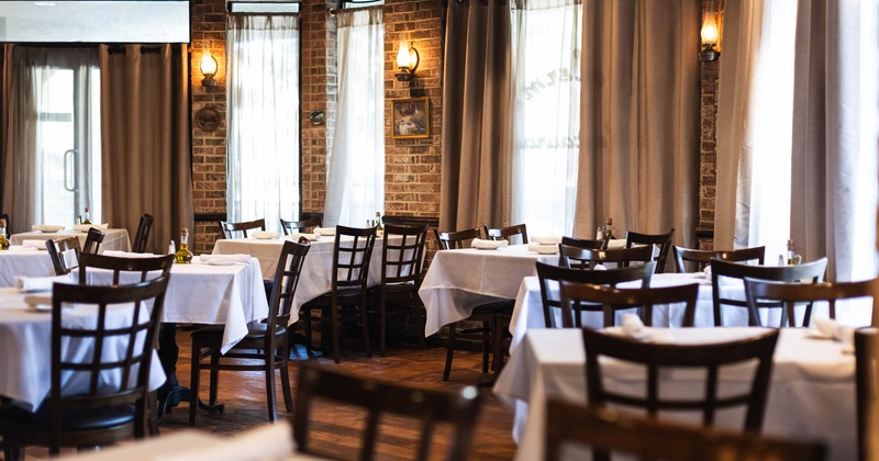 Interior dining area with white tablecloths, wooden chairs and brick walls