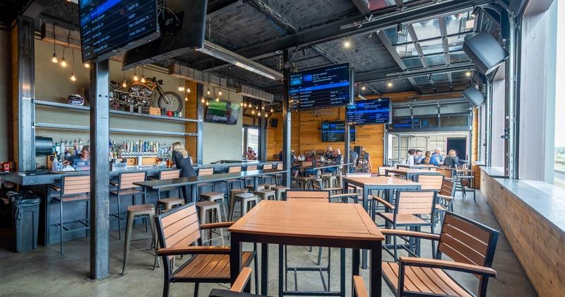 A modern bar with wooden tables and chairs, a long bar counter, hanging screens