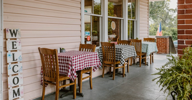 Outdoor porch with tables covered in checkered tablecloths and a "WELCOME" sign