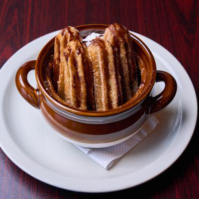 Freshly fried churros served in a traditional brown ceramic pot.