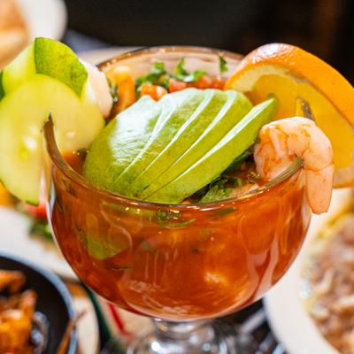 Shrimp cocktail with avocado slices, garnished with orange and cucumber slices.