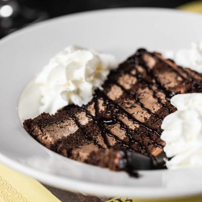 A slice of chocolate mouse cake with chocolate syrup drizzles and whipped cream.