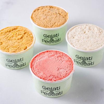 Four cups of gelato with different flavors on a white surface.