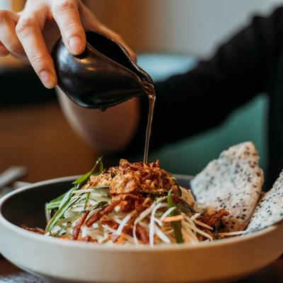 A hand pouring sauce over papaya salad.