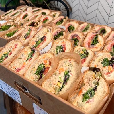 Catering platter of gourmet sandwiches arranged in a disposable box for serving.
