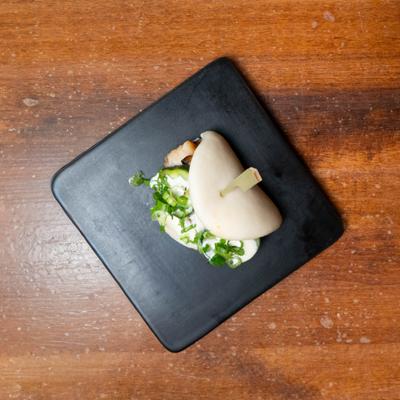 Bao bun with creamy sauce and scallions on a black plate.