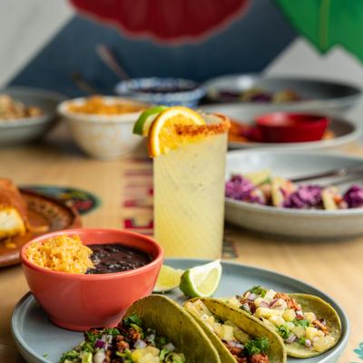 Chorizo tacos served with a side of black beans and lime wedges, alongside a cocktail.