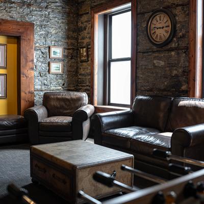 Rustic lounge room with leather furniture, stone walls, and windows.
