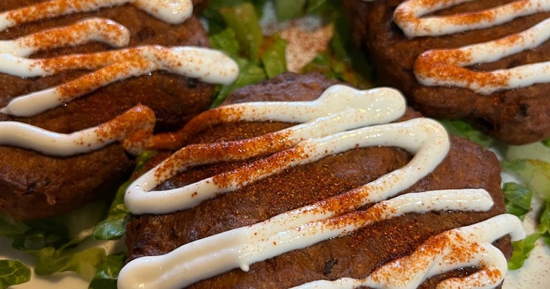 Pan-fried patties drizzled with sauce, served over greens