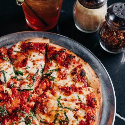 Margherita pizza on a table with a drink and condiments.