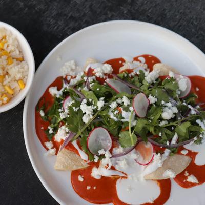 Enchiladas topped with sauces, greens, crumbled cheese and sliced radishes.