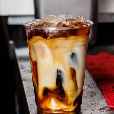Iced coffee layered with milk swirling inside a clear plastic cup.