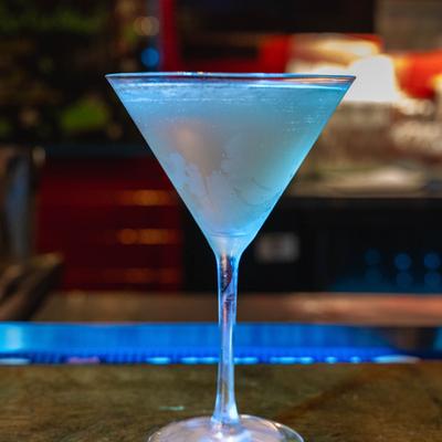 Martini cocktail in a stemmed glass on a blue-lit bar counter.