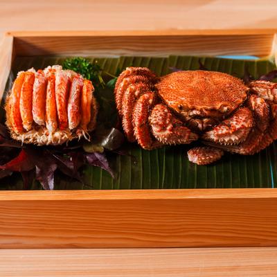 Whole crab and crab legs displayed on banana leaf in a wooden box.