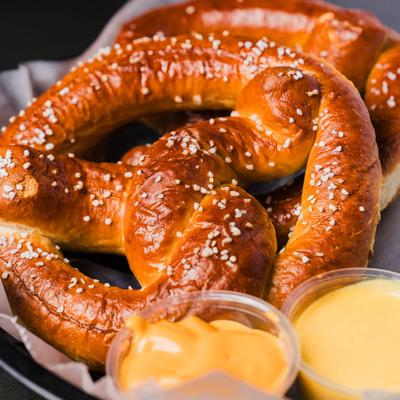 Two golden-brown pretzels  sit on a plate with small cups of cheese sauce.