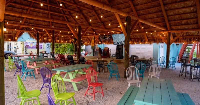 Covered outdoor seating area with colorful wooden chairs and tables and a music stage