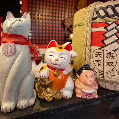 Japanese beckoning cat beside a grey cat statue and a small sumo statue.