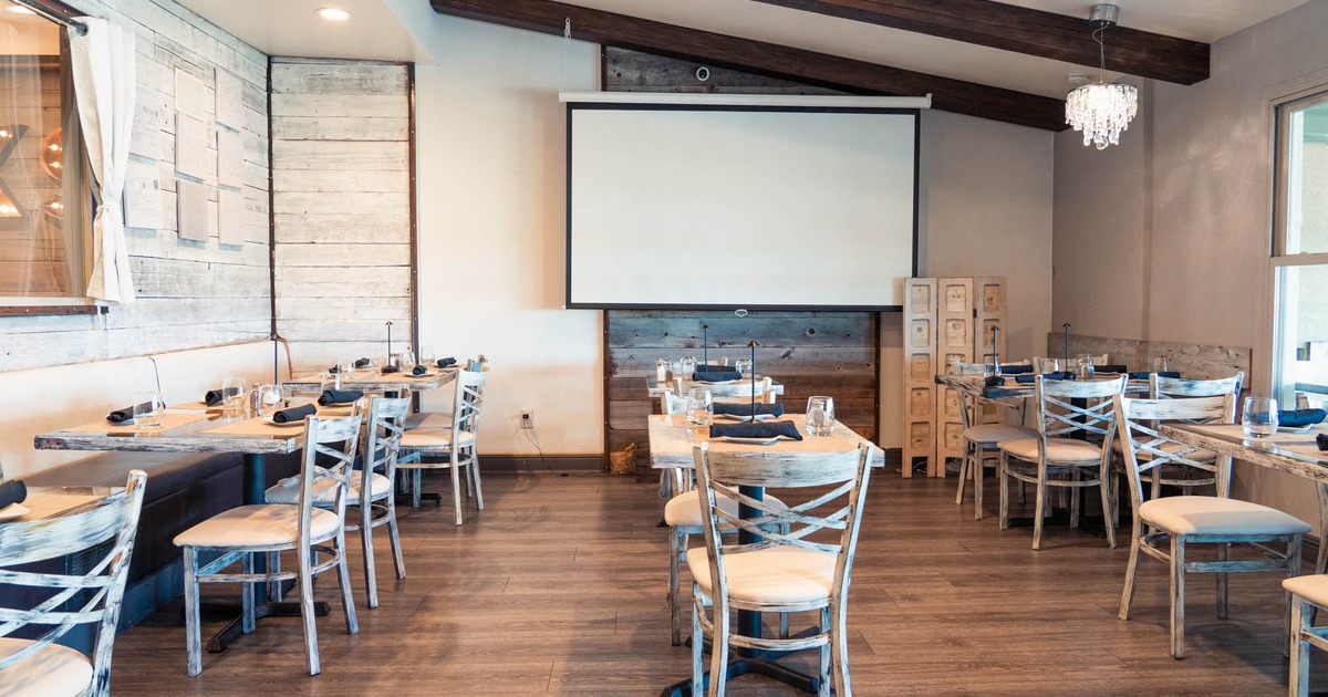 White room seating with set tables, banquette, chairs and a projection screen