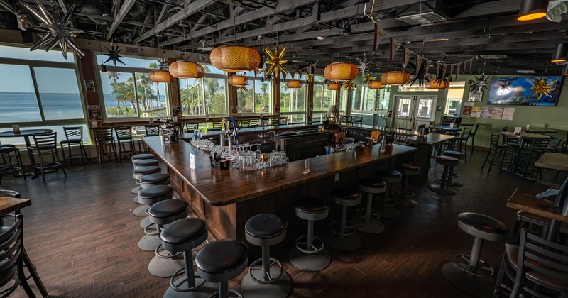 Interior view with a wooden counter, backless stools, large windows overlooking a waterfront