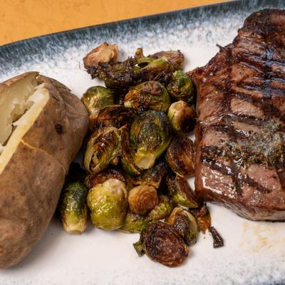 Grilled steak with crispy brussels sprouts and a baked potato.