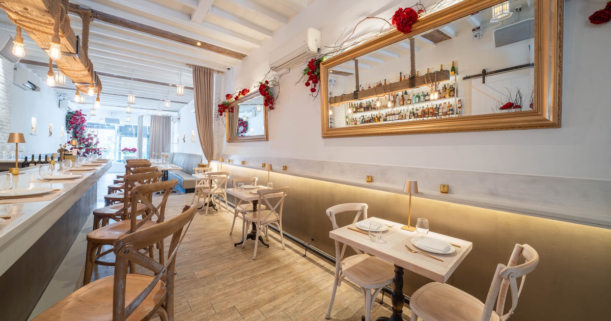 Elegant restaurant interior with bar stools, hanging lights, and tables against a softly lit wall
