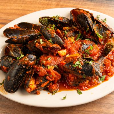 A white plate holds mussels in marinara sauce.