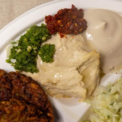 Latke served on a platter alongside hummu, tahini and condiments, close-up.