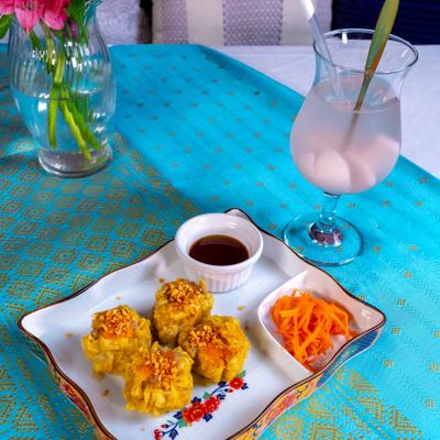 Steamed dumplings served with a dipping sauce, shredded carrots and a drink.