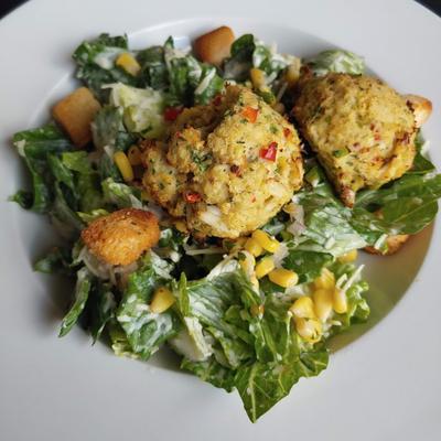 Caesar salad with corn salsa topped with two crab cakes.