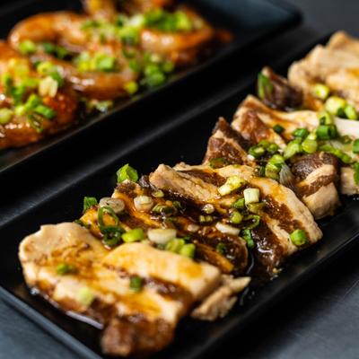 Marinated pork belly drizzled with a dark glaze and garnished with green onions.