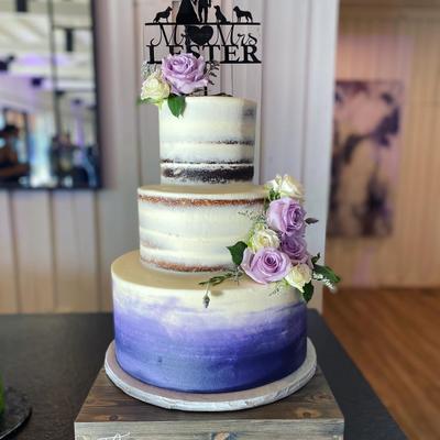 Three tier white and blue naked cake, garnished with purple roses
