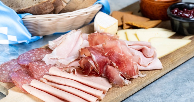 Charcuterie board with sliced meats and cheeses, alongside a basket of bread