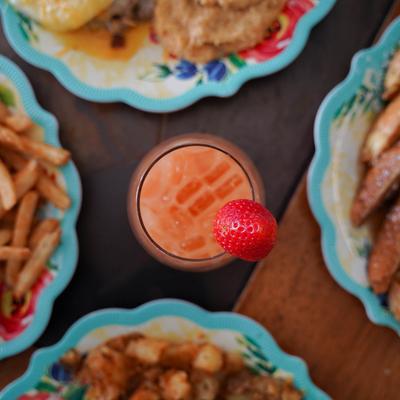 A refreshing drink topped with a strawberry, surrounded by plates of fried food and fries.