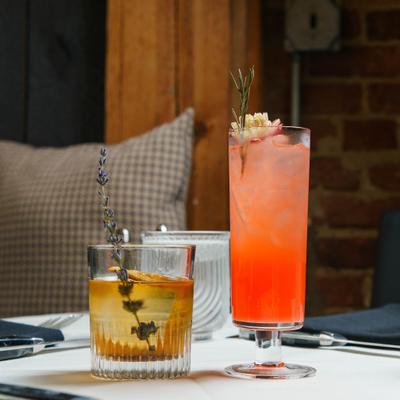 Two cocktails served in distinct glassware on a restaurant table.
